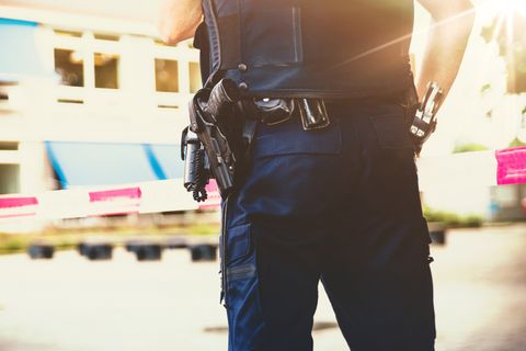 Politieagent met uitrusting aan het koppel, staand achter afzetlint op een plaats delict