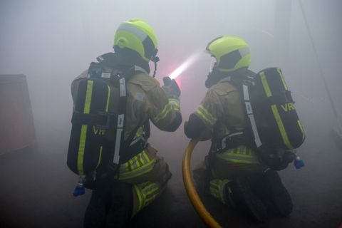 Twee brandweerlieden met ademluchtapparatuur tijdens een inzet in dichte rook